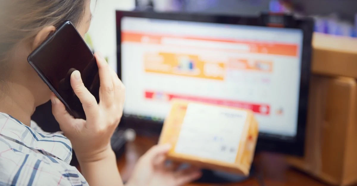 Mulher realizando várias tarefas ao mesmo tempo, usando um telefone e verificando um pacote de compra on-line em casa. Contexto: