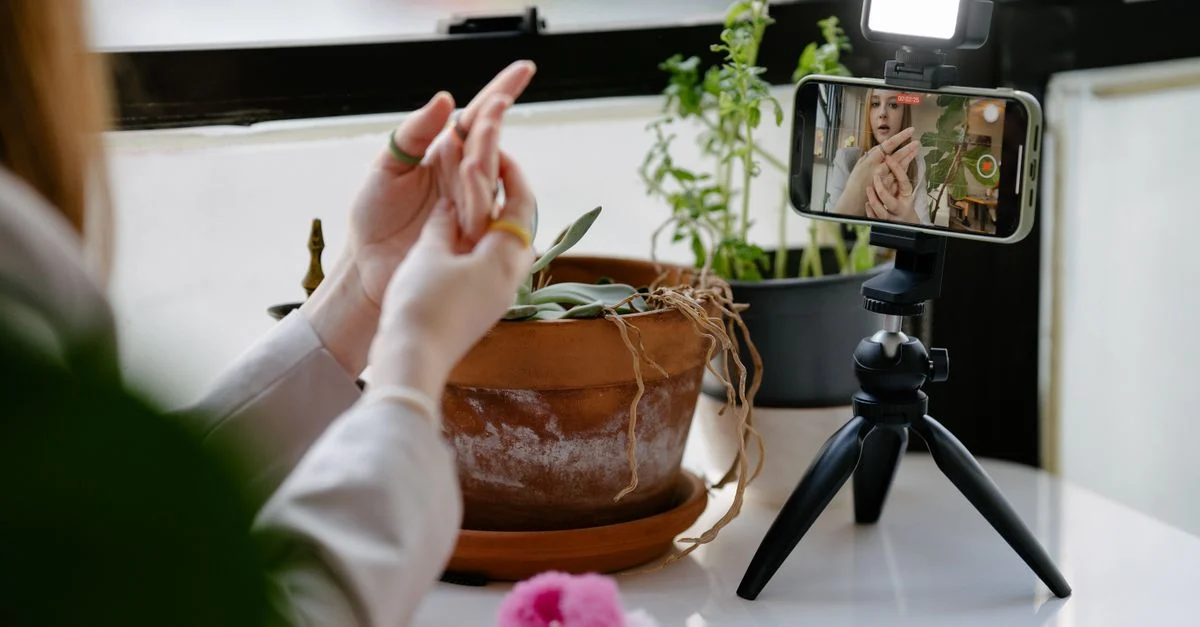Uma mulher usa um smartphone montado em um tripé para gravar um vídeo em um ambiente interno com plantas ao fundo. Contexto: Afiliados no TikTok Shop: como funciona para marcas e creators