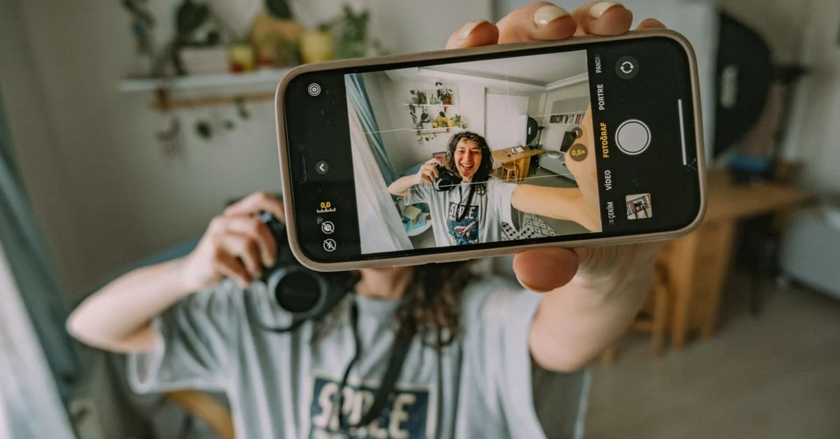 Uma pessoa tira uma selfie com um smartphone em um quarto aconchegante e cheio de plantas. Contexto: Creator Ads: como usar conteúdo de criadores em mídia paga
