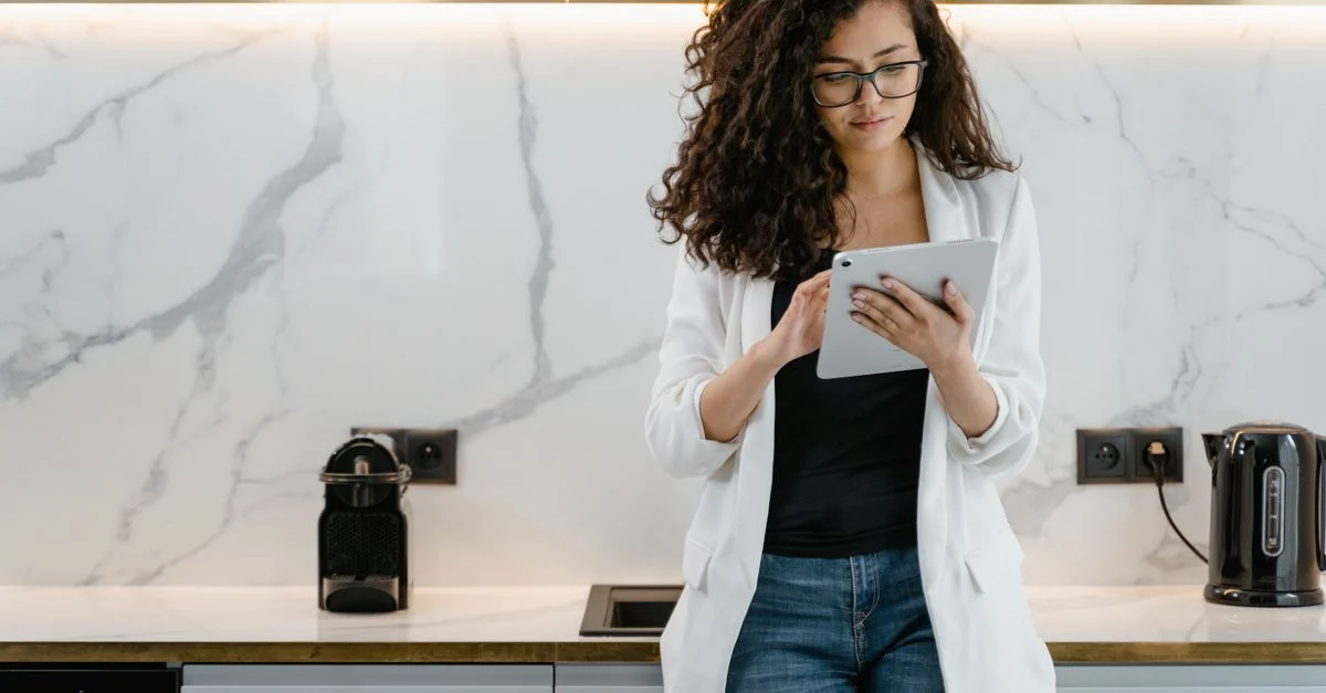 Mulher em um blazer branco usando um tablet em um ambiente de cozinha contemporâneo. Contexto: Criativos para tráfego pago: formatos, testes e otimização
