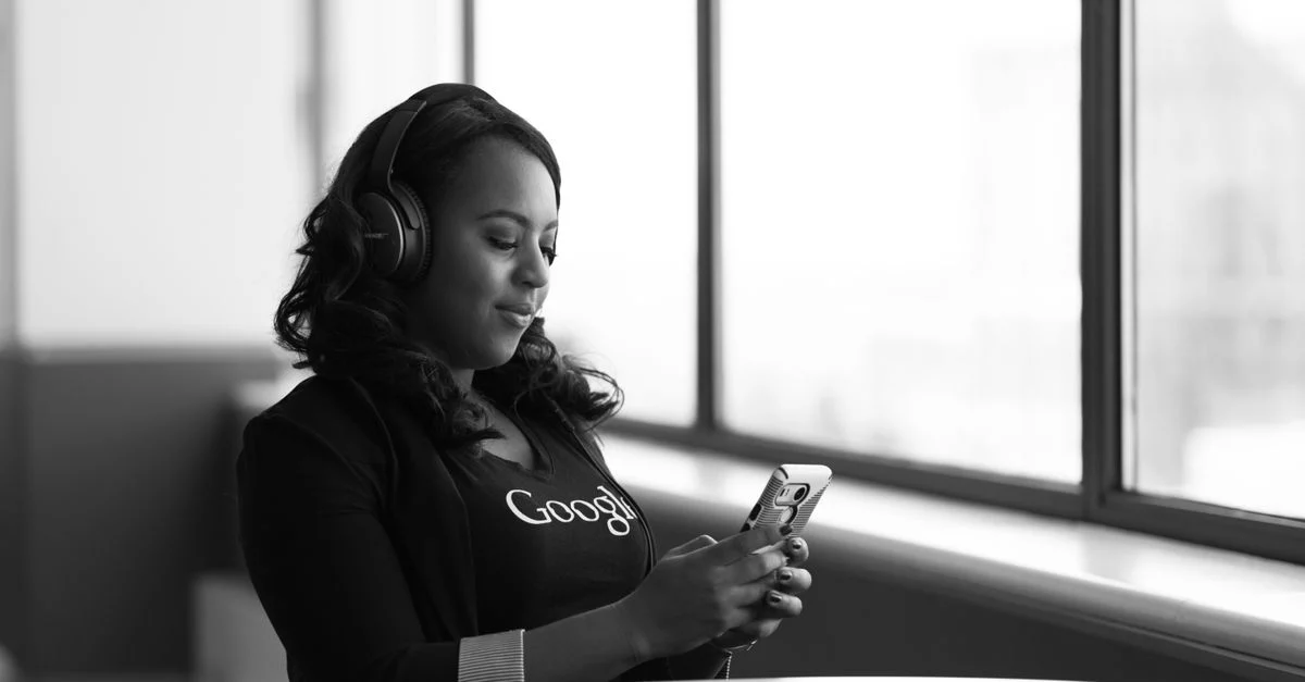 Jovem mulher sentada ao lado de uma janela, usando um smartphone com fones de ouvido, aproveitando momentos de lazer em casa. Contexto: Follow-up automático no WhatsApp: fluxos e exemplos