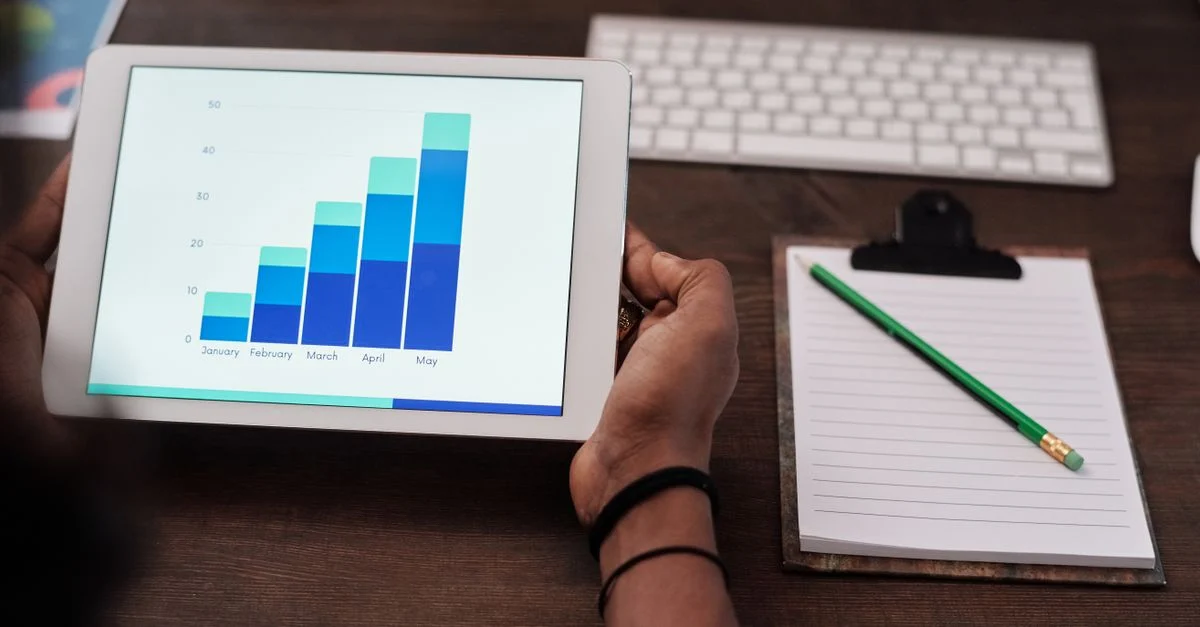 Close-up de uma pessoa segurando um tablet exibindo gráficos de crescimento em uma mesa de madeira. Contexto: Landing page para tráfego pago: como aumentar a conversão