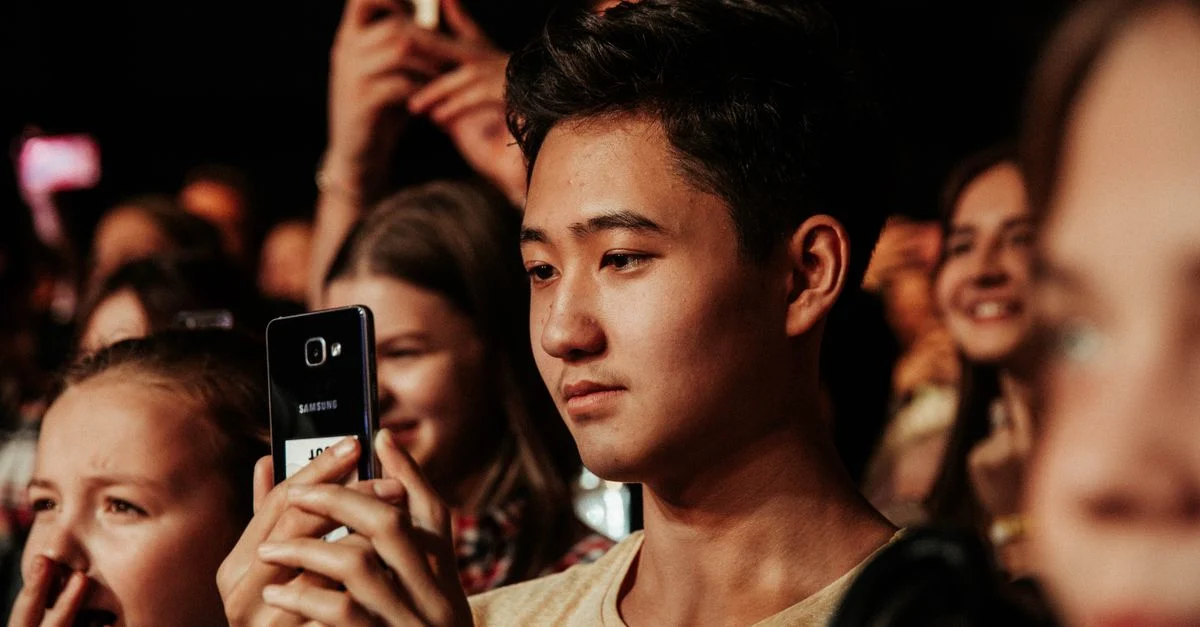 Um grupo de jovens na plateia capturando momentos memoráveis com smartphones. Contexto: Marketing de Influência: estratégia, custos e resultados