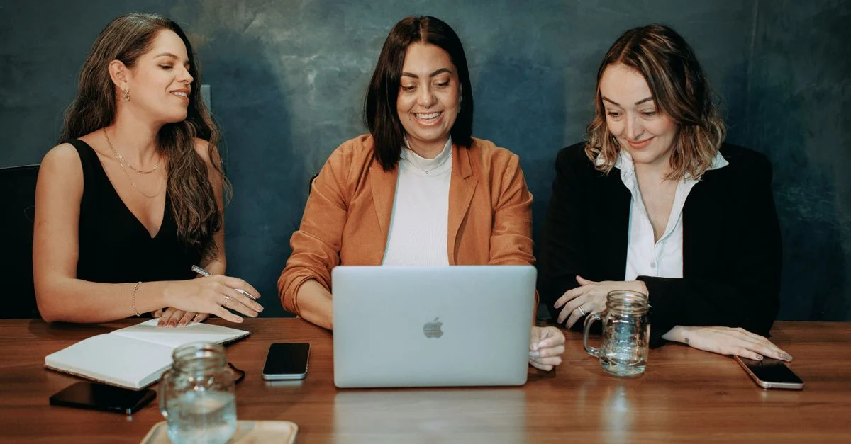 Três mulheres envolvidas em uma reunião de negócios em torno de um laptop, demonstrando trabalho em equipe e colaboração. Contexto: Marketing de performance: o que é e como medir resultados