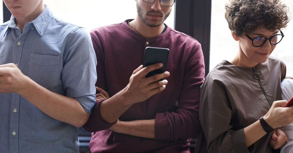 Um grupo diverso de pessoas usando smartphones ativamente em ambientes internos. Tecnologia moderna e interação social. Contexto: Marketing Digital: o que é e como usar para crescer