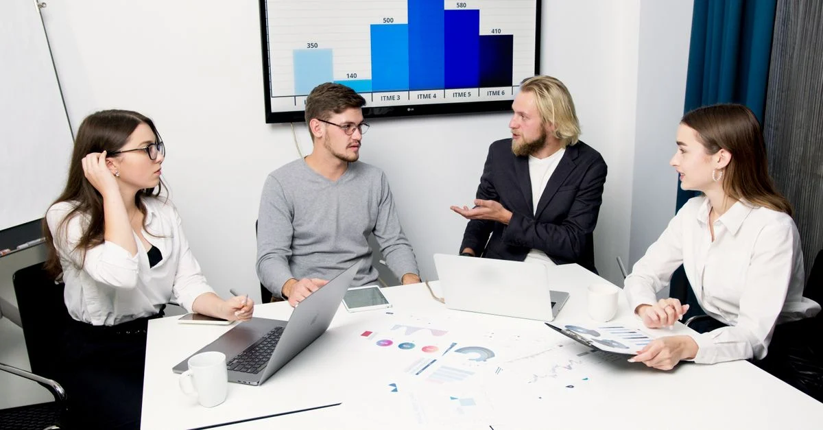 Um grupo de profissionais de negócios discutindo dados em uma mesa de reunião com laptops e gráficos. Contexto: Plano de marketing digital: como montar uma estratégia prática