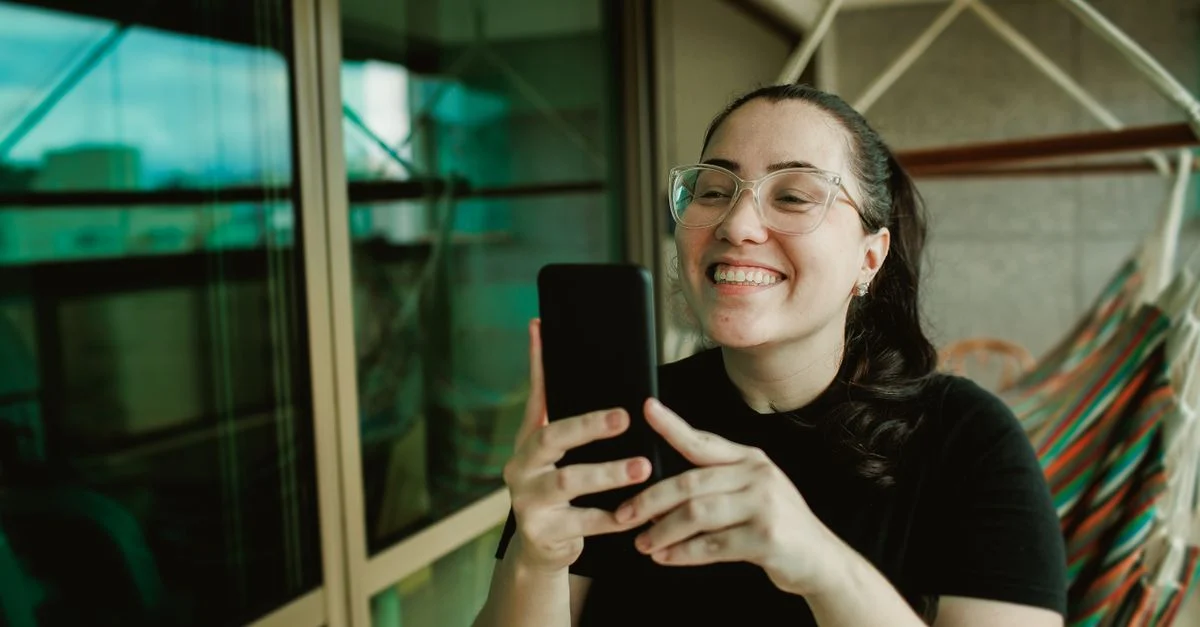 Mulher alegre usando smartphone em uma varanda, curtindo um momento relaxado em casa. Contexto: Quanto custa contratar um influenciador? Preços e fatores