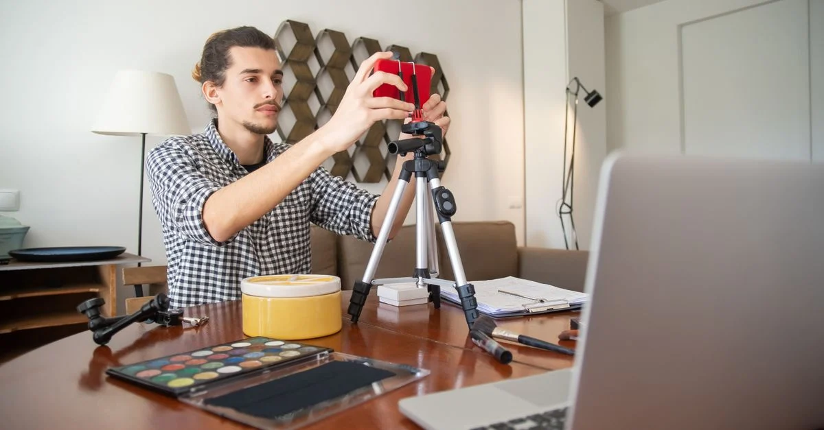 Um vlogger masculino ajusta sua câmera em um tripé, se preparando para uma gravação em um estúdio doméstico estiloso. Contexto: Roteiro UGC: como criar vídeos que prendem atenção e convertem