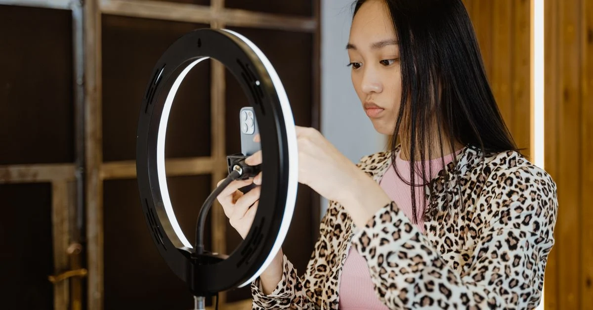 Mulher asiática com jaqueta de estampa de leopardo ajusta luz de anel para configuração de streaming no smartphone. Contexto: Social Commerce: o que é e como vender nas redes sociais