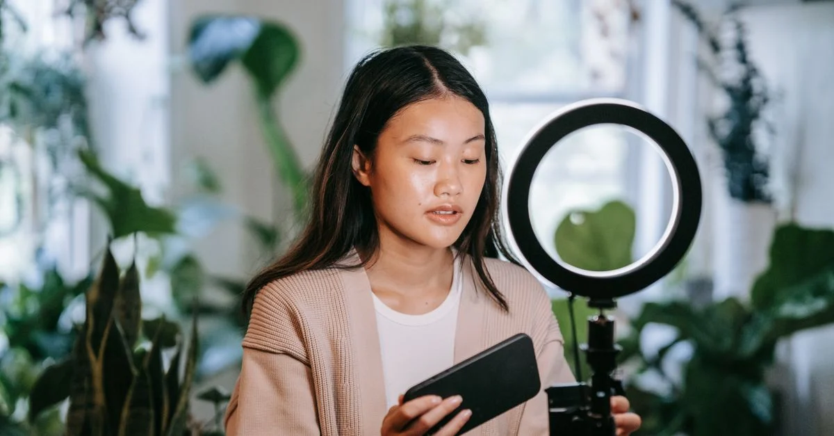 Mulher asiática ajustando smartphone e luz de anel em ambiente interno para gravação de vídeo. Contexto: Taxas do TikTok Shop no Brasil: comissão, tarifa e margem
