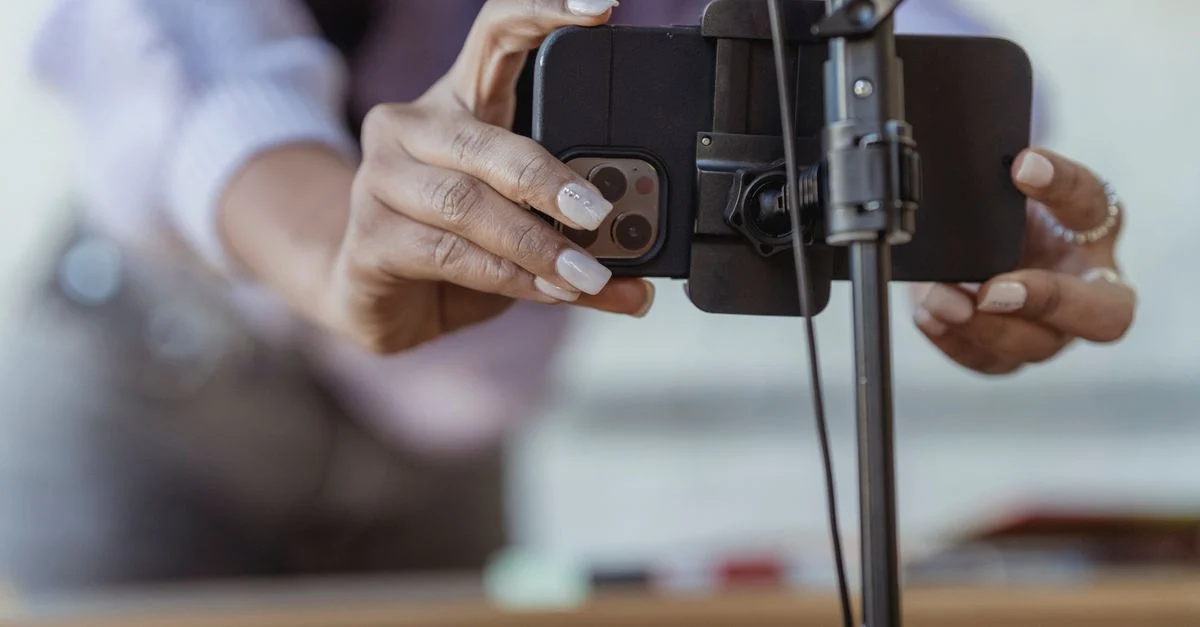 Uma pessoa configura um smartphone em um tripé para gravação de vídeo ou transmissão ao vivo dentro de casa. Contexto: UGC: o que é e como usar conteúdo de criadores em campanhas