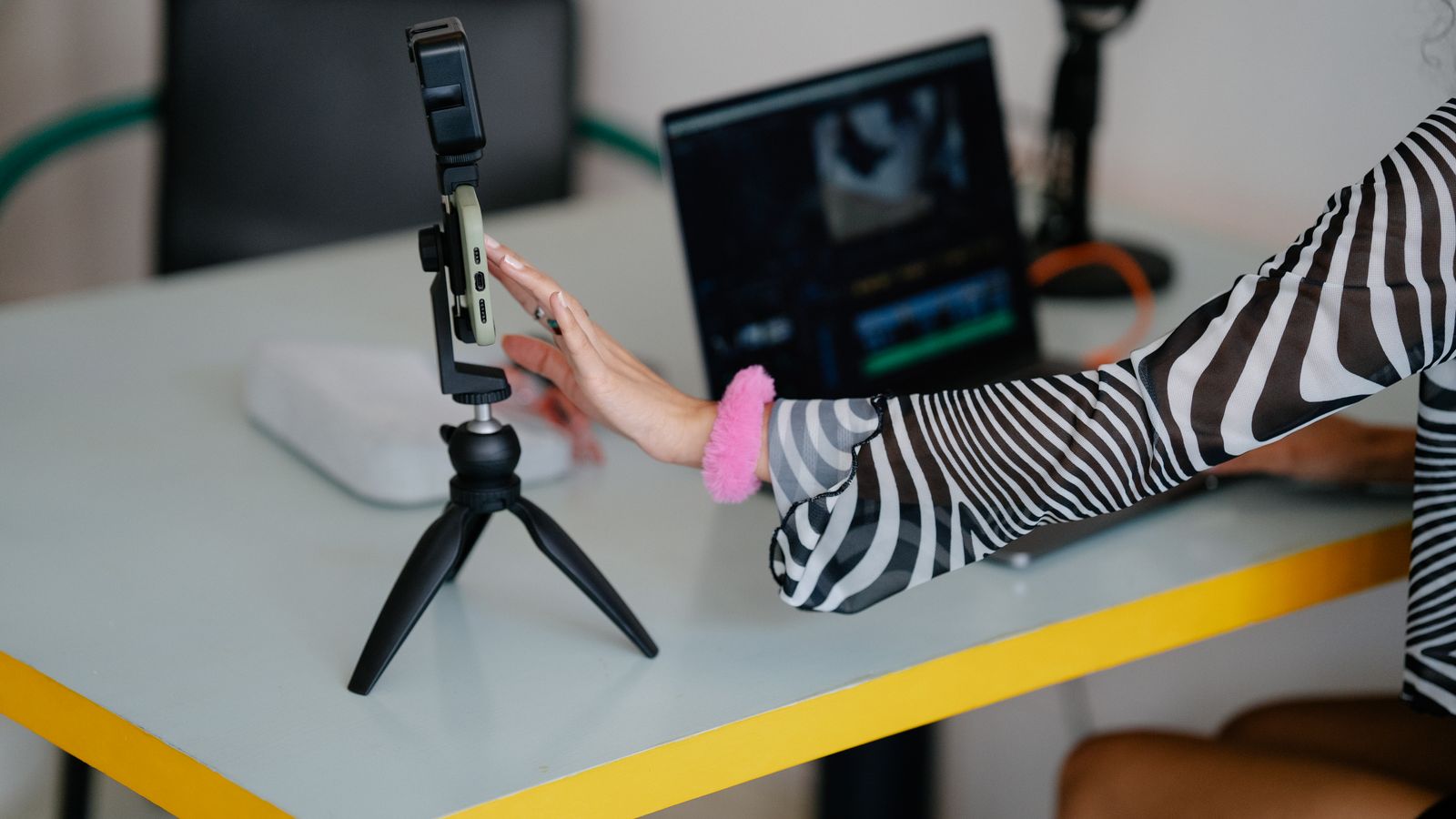 Creator ajustando smartphone em tripé ao lado de notebook para produção de vídeo